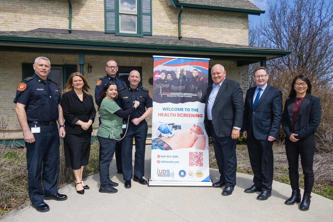 City staff and fire chiefs standing beside a "Welcome to the Health Screening" sign.