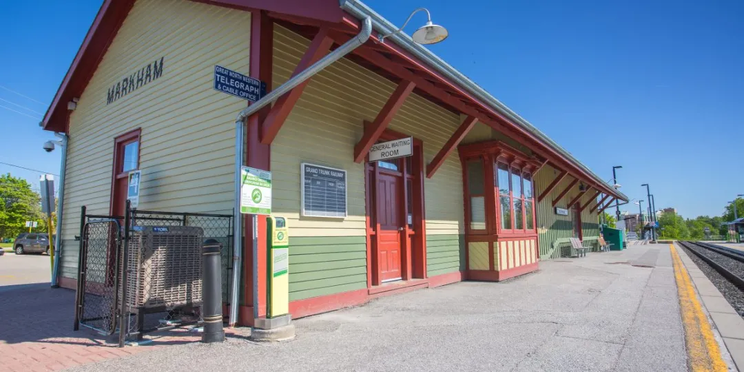 Exterior of the Markham Village Train Station with light siding, red trim, and a railway platform.